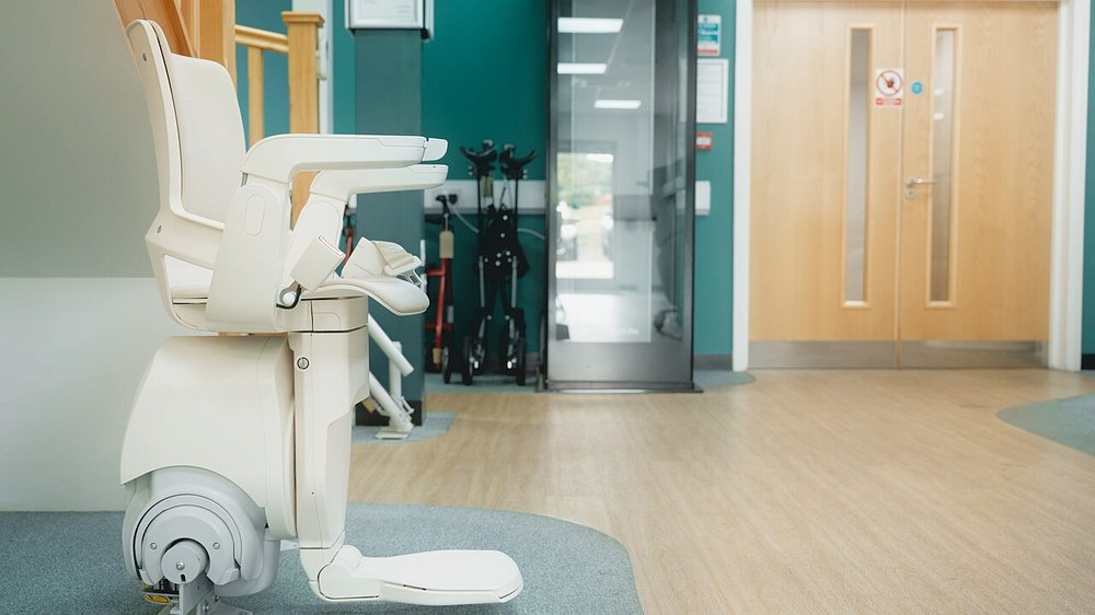 A white chair stairlift with a folding footrest parked at the foot of a staircase